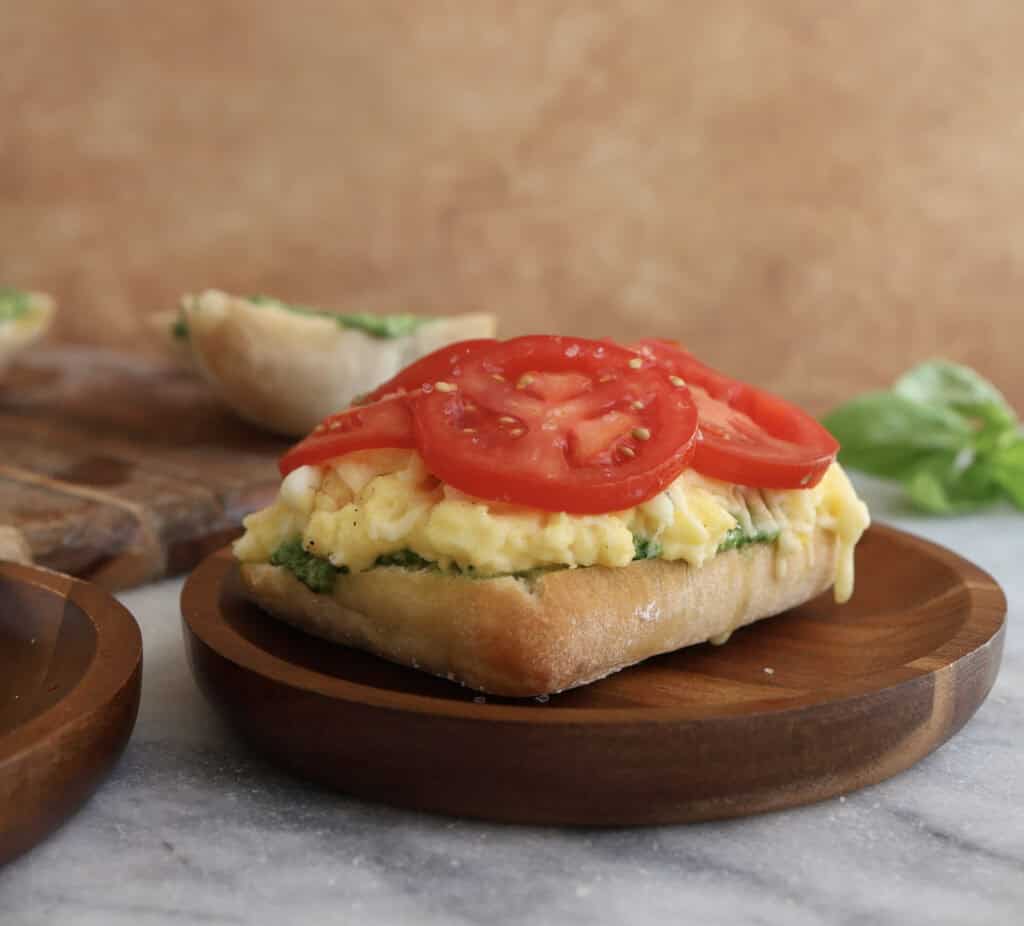 Open spinach pesto egg sandwich on a wood plate, showing the sliced tomatoes.