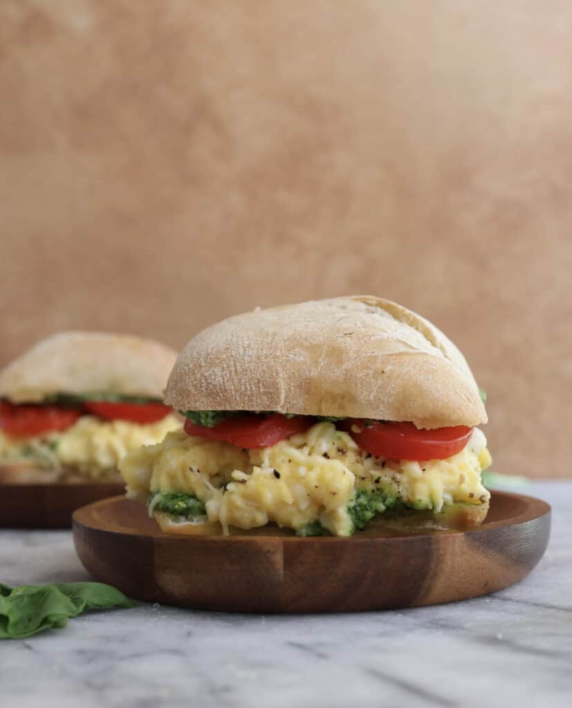 Side view of the egg sandwich with spinach pesto sitting on a wood plate.