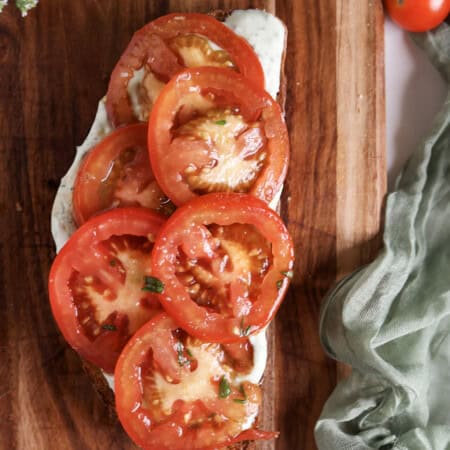 Marinated tomato and ricotta toast on a cutting board.