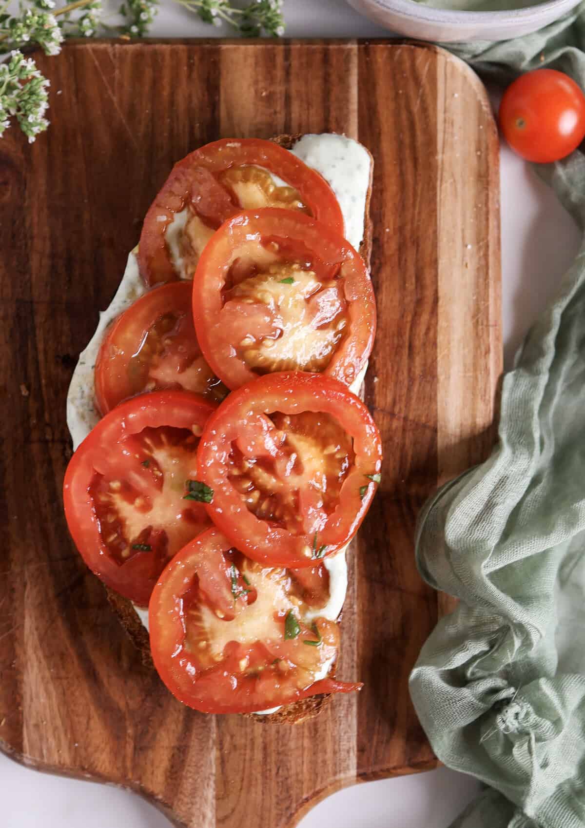 Marinated tomato and ricotta toast on a cutting board.