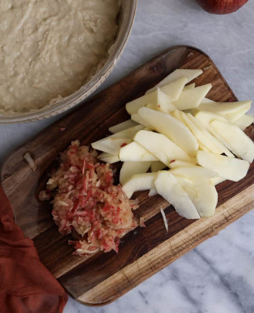 Thinly sliced apples and grated apples on a wood cutting board for the apple coffee cake. 