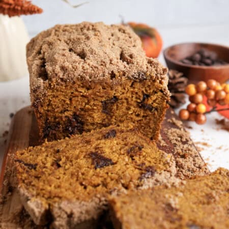 Sliced pumpkin chocolate chip bread with crumb topping on a wood cutting board.