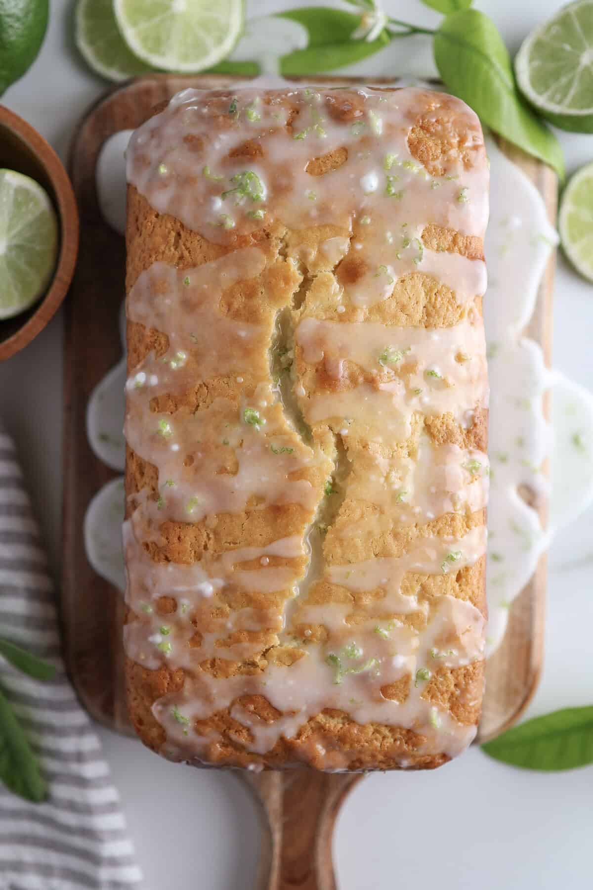 Lime loaf cake with simple lime glaze drizzled over it on a cutting board.