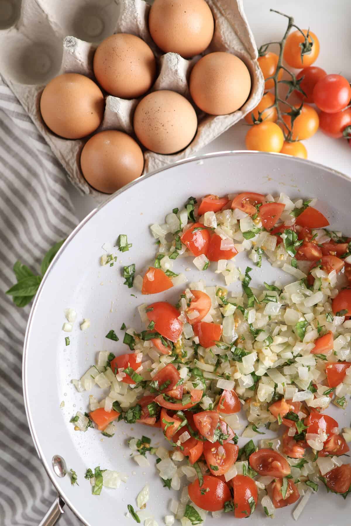 The sauteed onions with tomatoes and basil in a skillet before being added to the egg bites. 
