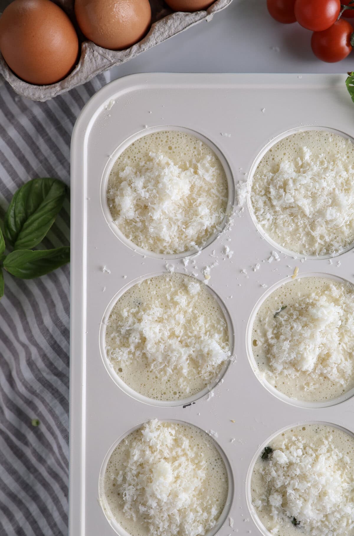 Ricotta egg bite mixture in muffin tin with parmesan cheese on top before being baked.