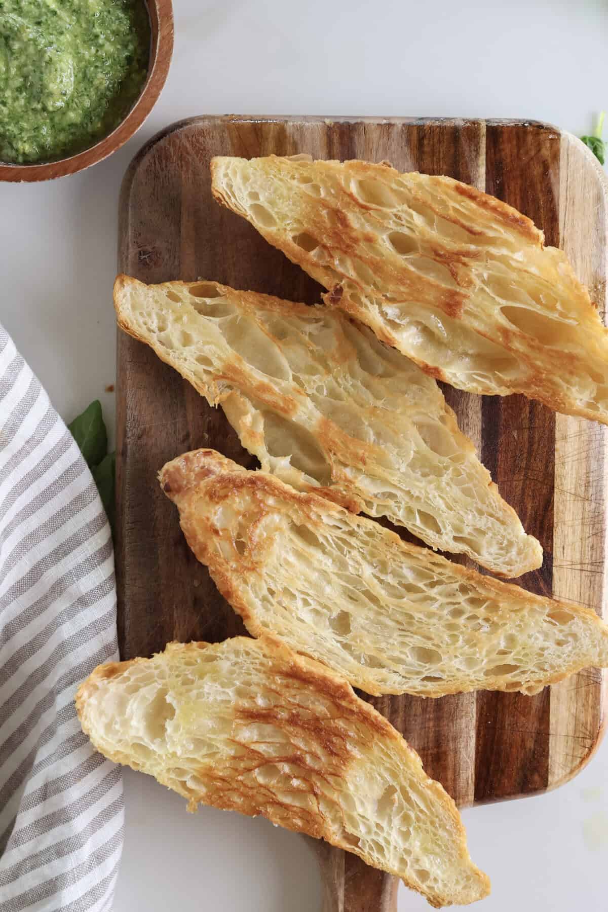 Sliced and toasted croissants for the breakfast sandwiches with a bowl of pesto sitting near by. 
