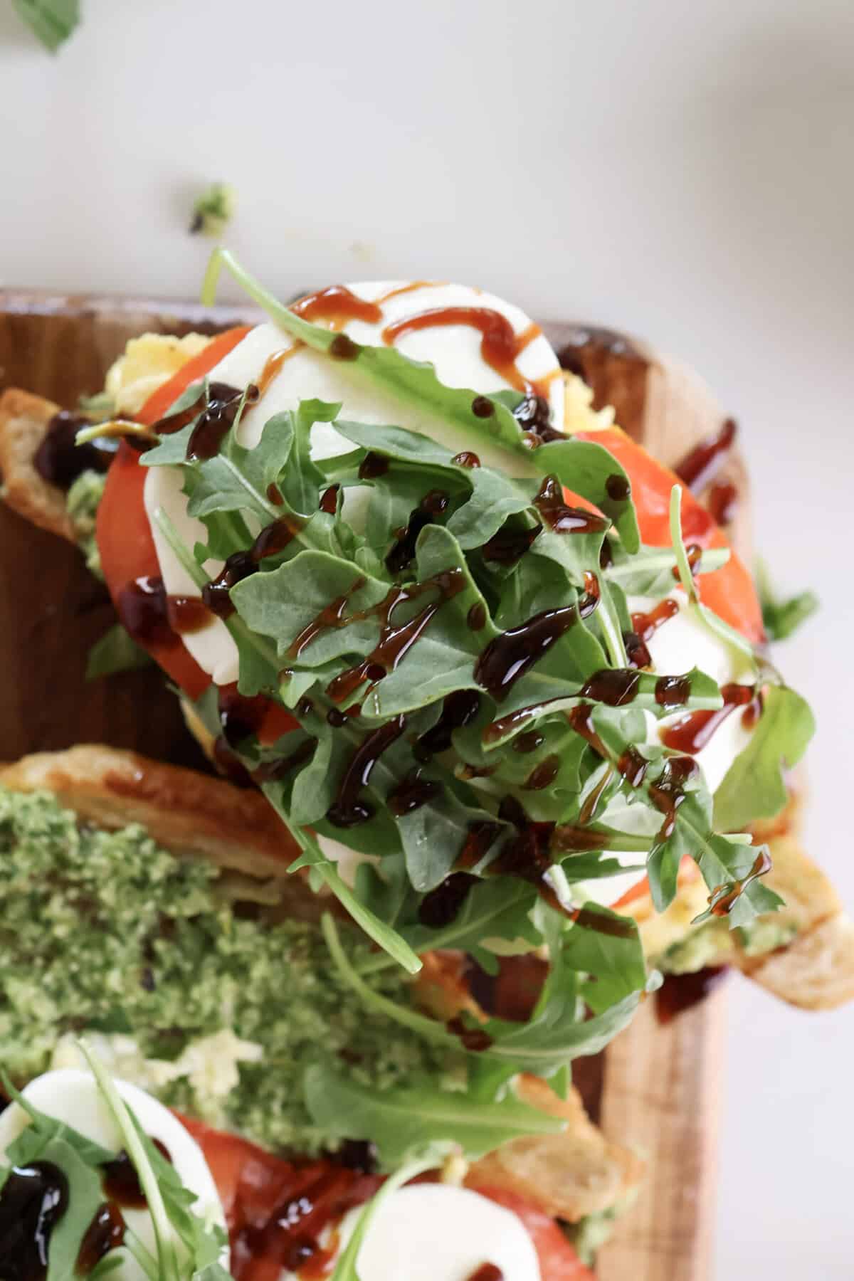Up close shot an open caprese croissant breakfast sandwich showing a drizzle of balsamic glaze over the sandwich. 