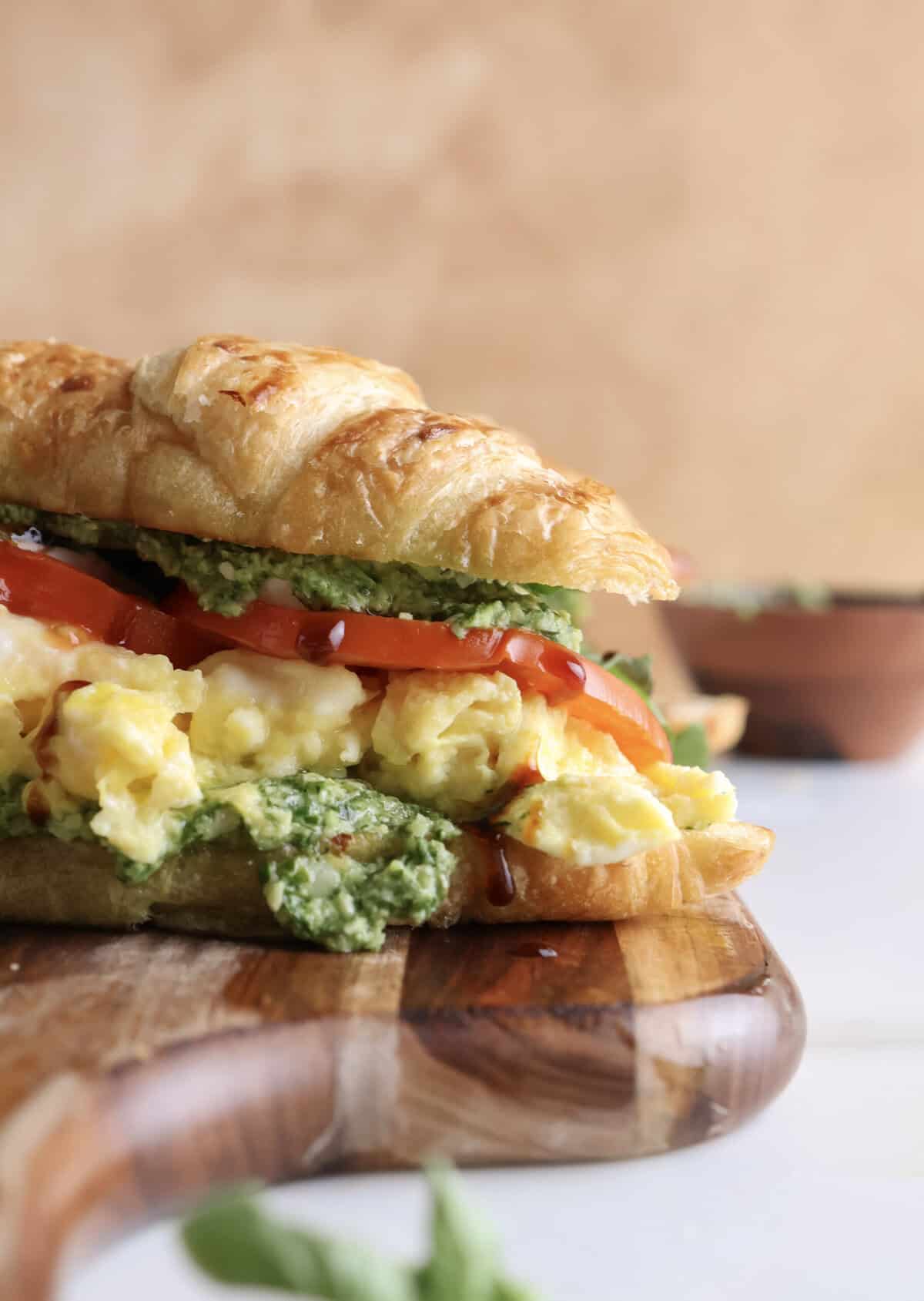 Side view of the croissant sandwich showing the layers of pest, scrambled eggs, tomatoes, cheese and arugula. 