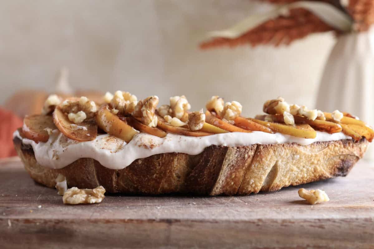 Sourdough toast topped with protein Greek yogurt, sauteed cinnamon apples and walnuts on a cutting board.
