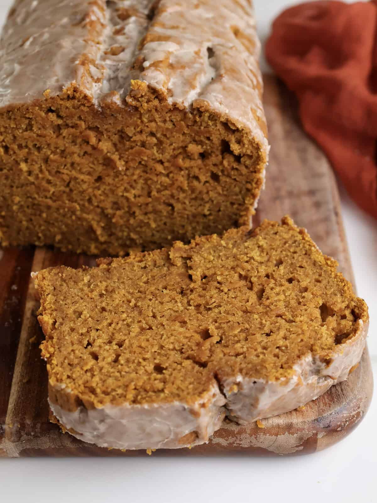 Spiced Pumpkin Bread loaf on cutting board with slice cut.
