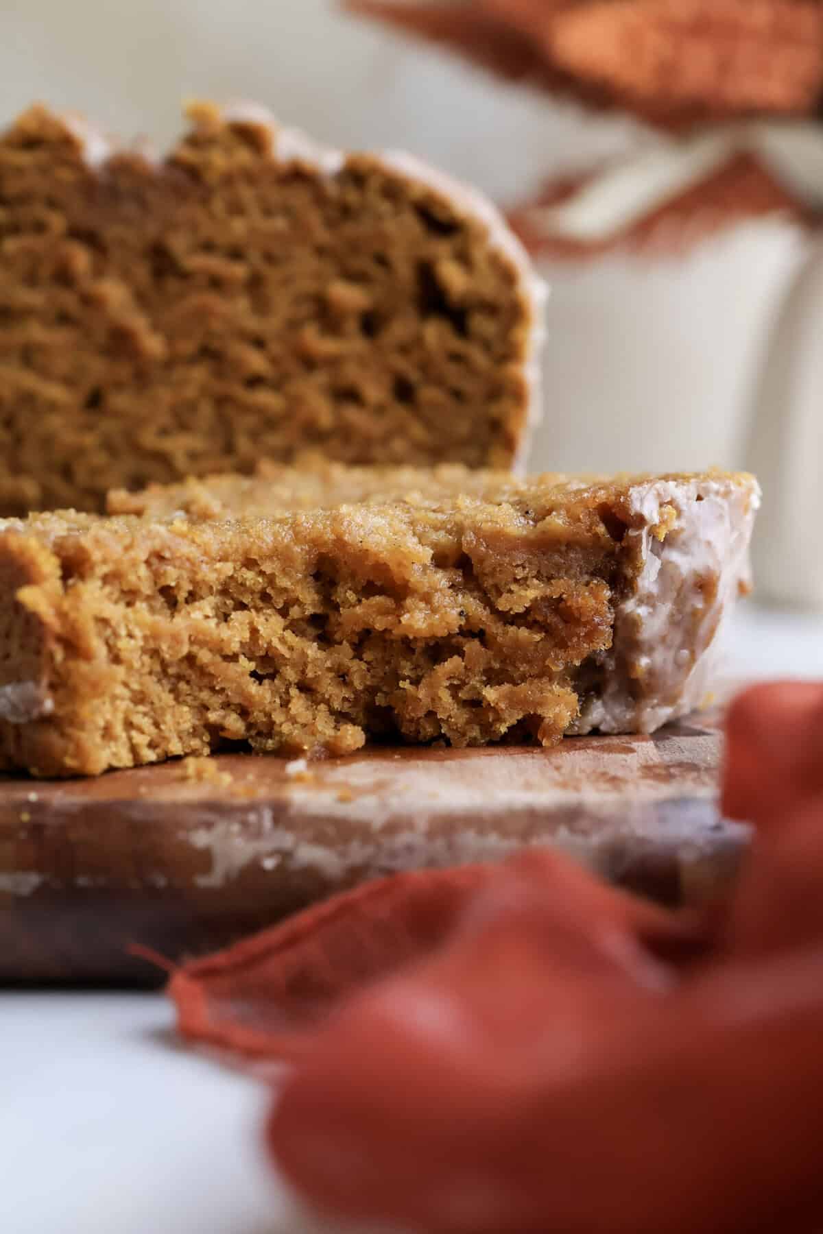 up close shot of a slice of the spiced pumpkin bread with cinnamon glaze on a cutting board.