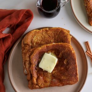 Two cream cheese stuffed pumpkin french toast slices with a pat of butter.