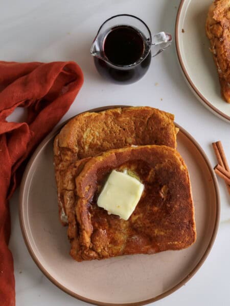 Two cream cheese stuffed pumpkin french toast slices with a pat of butter.