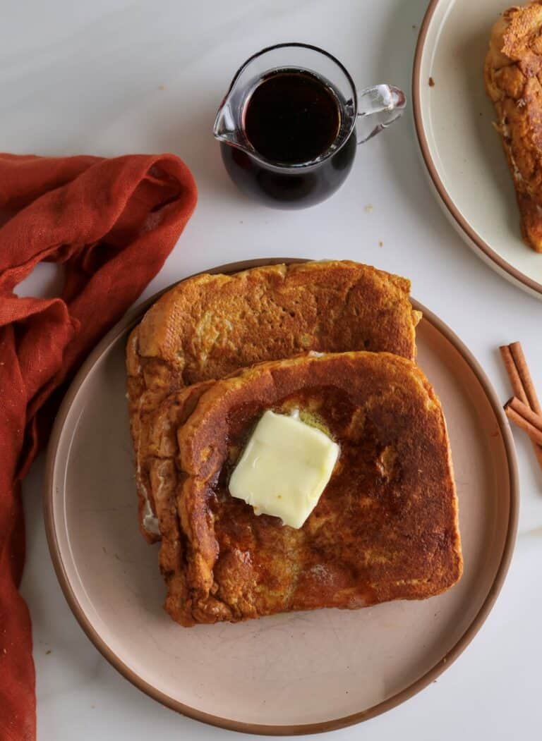 Two cream cheese stuffed pumpkin french toast slices with a pat of butter.
