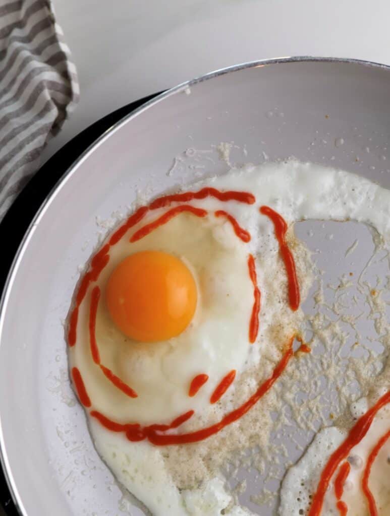 Egg in skillet cooking with parmesan cheese and drizzle of sriracha.