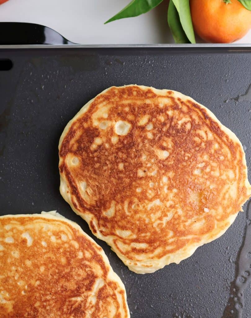 A golden brown ricotta orange pancake on the griddle after flipping.