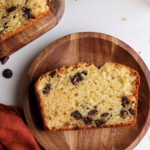 A slice of orange and chocolate chip loaf cake on a wooden plate.