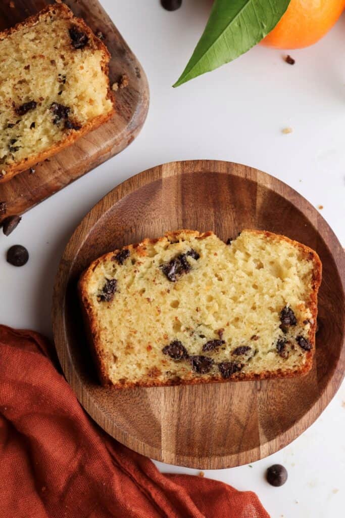 A slice of orange and chocolate chip loaf cake on a wooden plate.