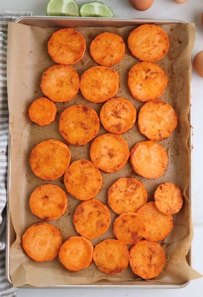 Seasoned sweet potato slices on baking sheet ready to be roasted.