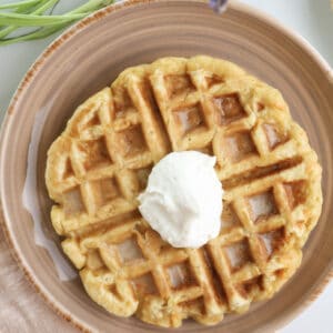 Carrot cake waffle with dollop of maple cream cheese on a plate.