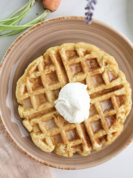 Carrot cake waffle with dollop of maple cream cheese on a plate.