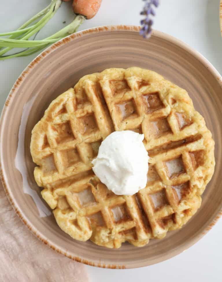 Carrot cake waffle with dollop of maple cream cheese on a plate.