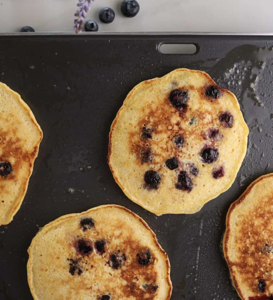Cornmeal blueberry pancakes cooking on the griddle.