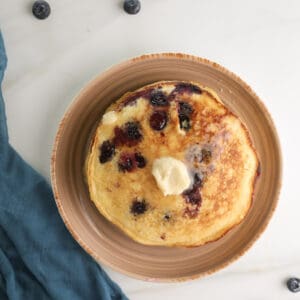 Overhead picture of a stack of cornmeal blueberry pancakes with honey butter.