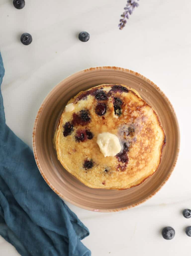 Overhead picture of a stack of cornmeal blueberry pancakes with honey butter.