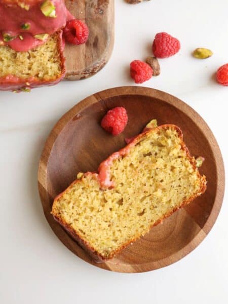 Slice of lemon pistachio loaf cake raspberry glaze on a plate.