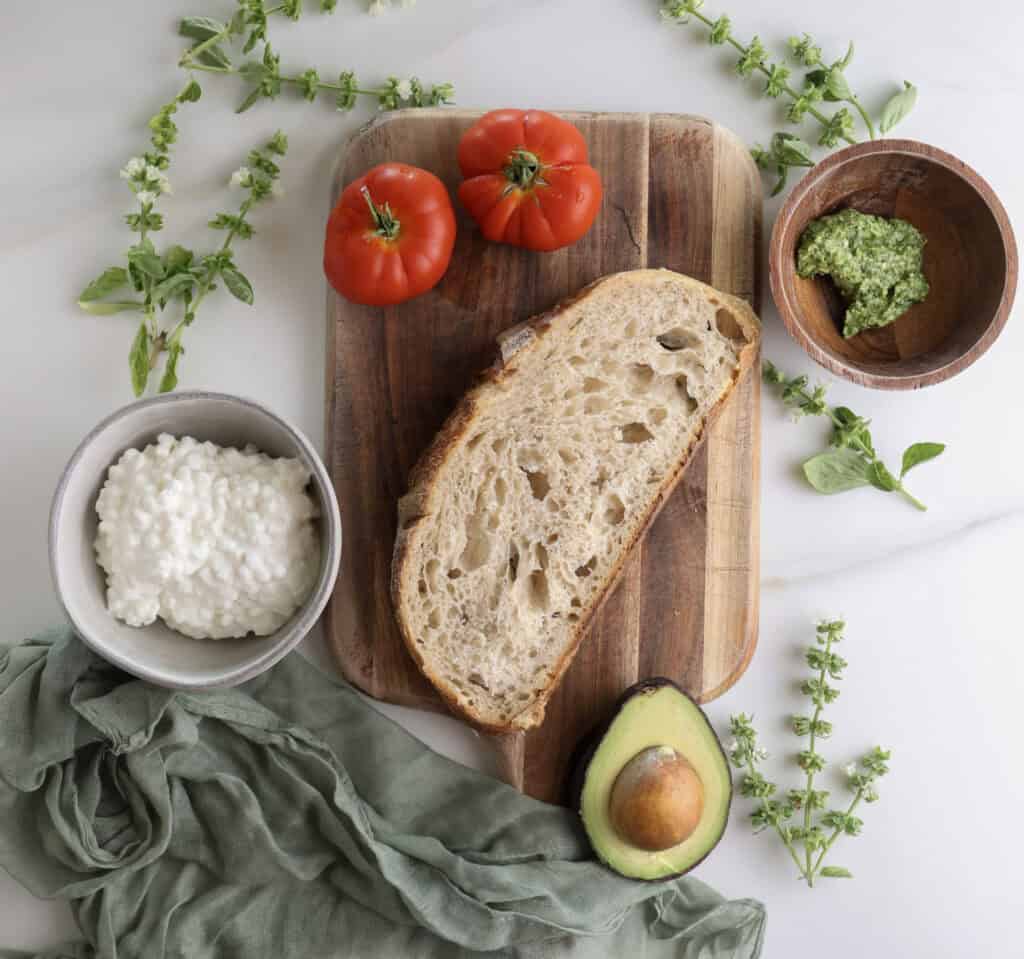 The ingredients on a counter needed to make the high protein avocado toast with tomatoes and pesto. 