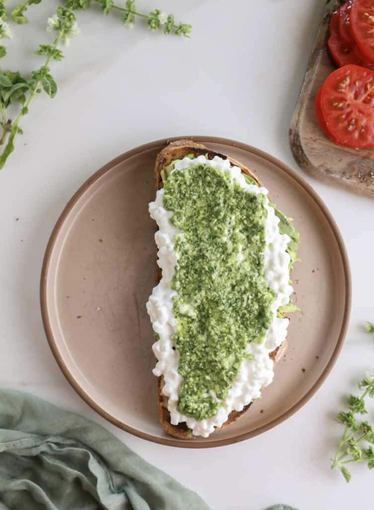 Pesto spread over the cottage avocado toast on a plate.