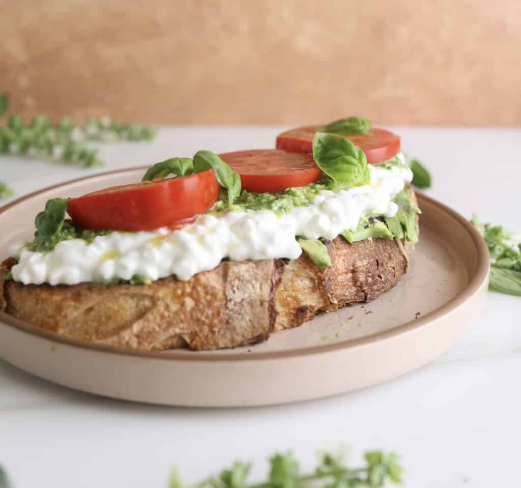 Up close side view of the cottage cheese avocado toast with tomatoes on a plate. 