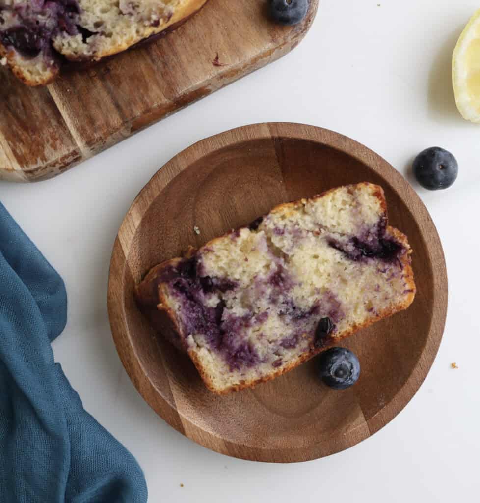 Lemon blueberry swirl loaf cake slice on a wood plate.
