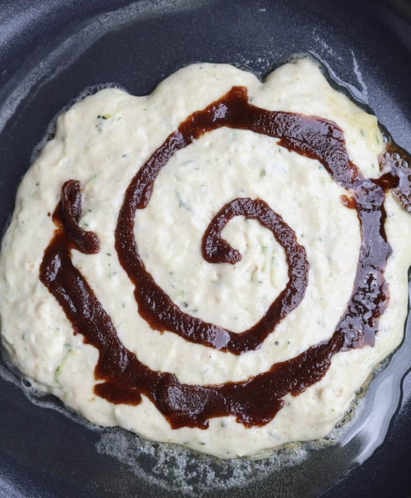 A cinnamon roll zucchini pancake in a skillet cooking with the cinnamon sugar butter swirl. 