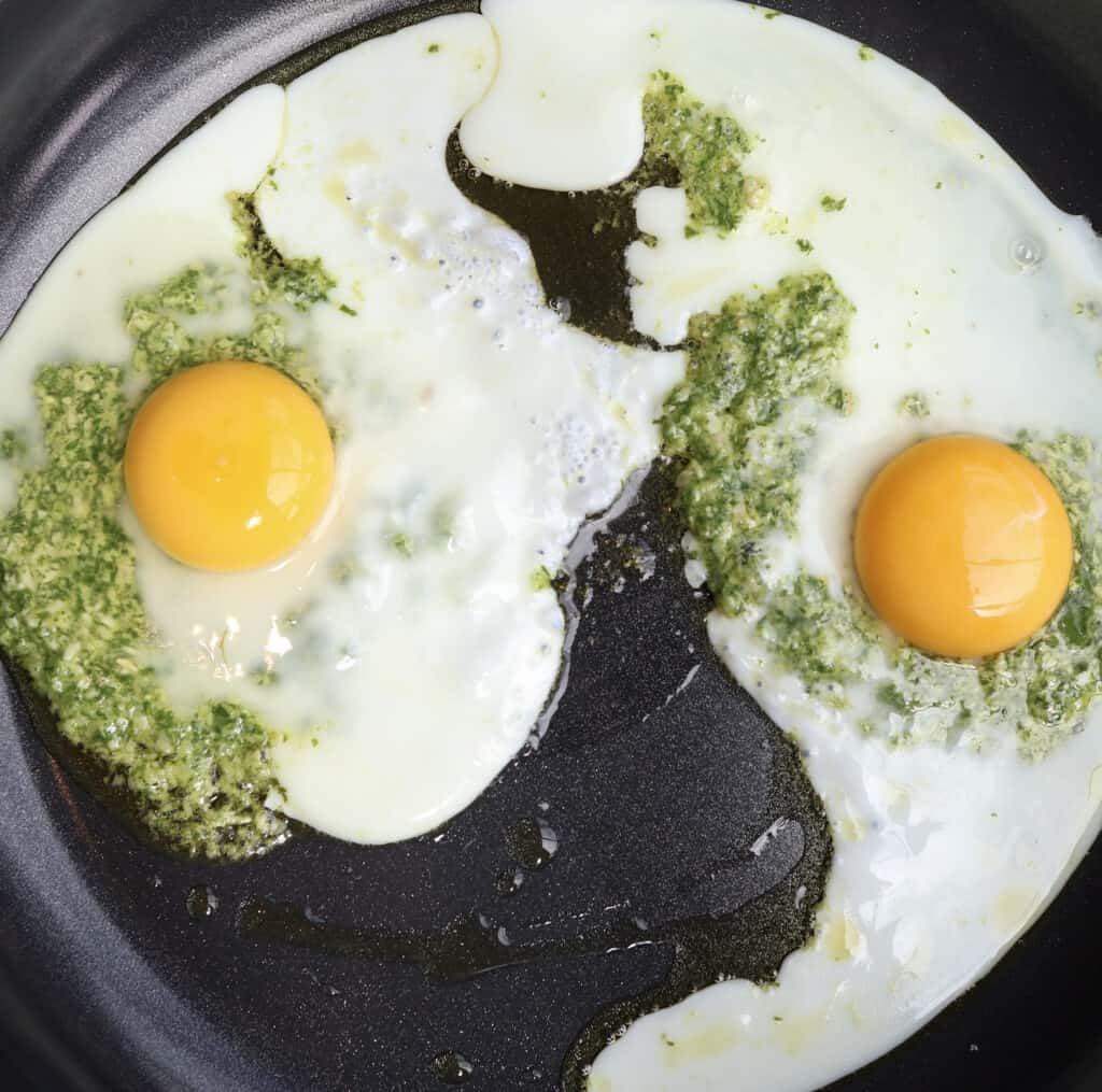 Pesto fried eggs cooking in a skillet. 