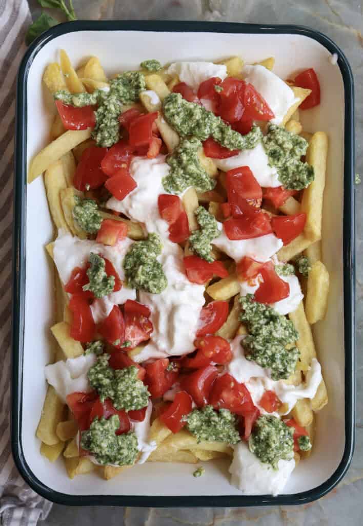 Caprese Breakfast French Fries with burrata, tomatoes and pesto spread out on a serving plate over the crispy fries. 