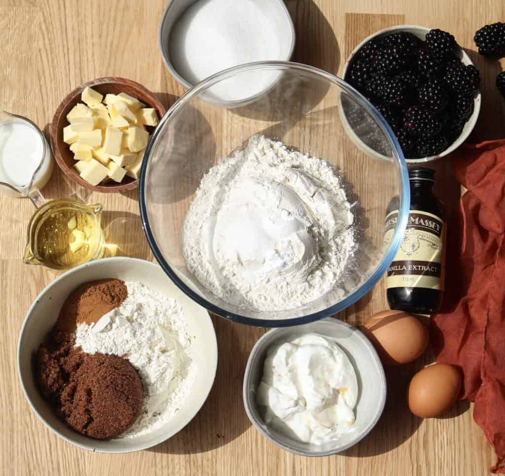 All the ingredients to make blackberry coffee cake on a wood counter.