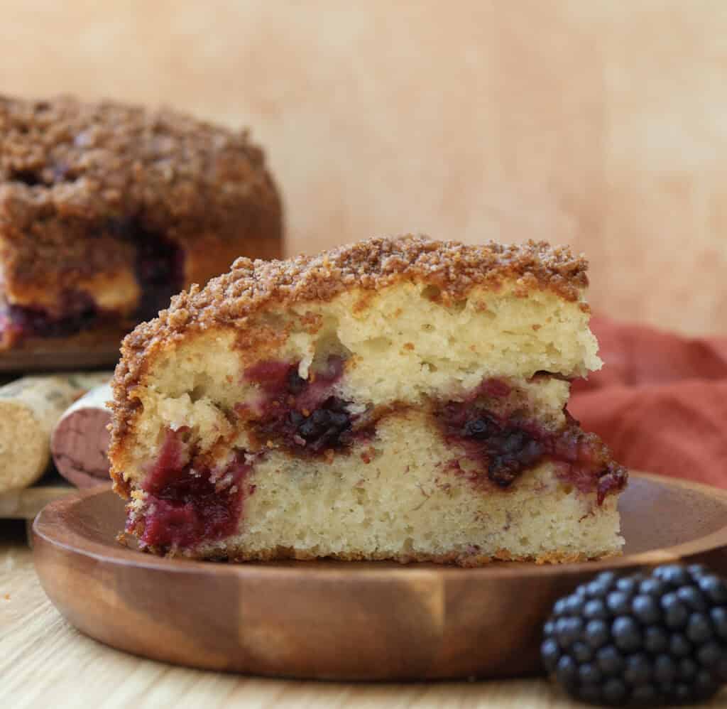 Slice of blackberry coffee cake with streusel on a wood plate.