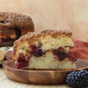 Slice of blackberry coffee cake with streusel on a wood plate.