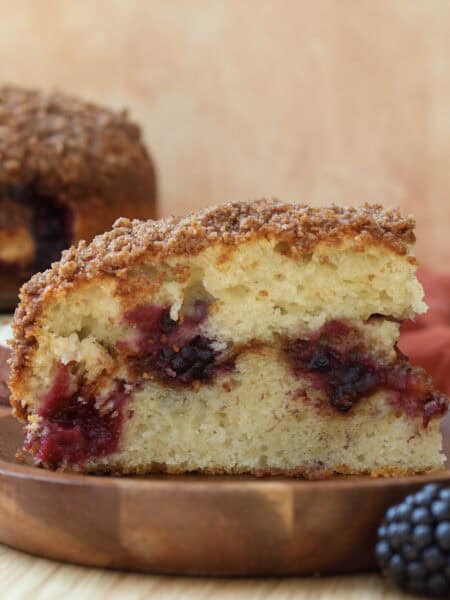 Slice of blackberry coffee cake with streusel on a wood plate.