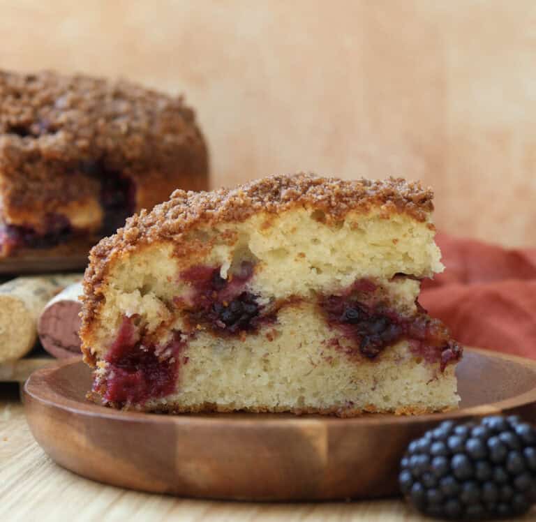 Slice of blackberry coffee cake with streusel on a wood plate.