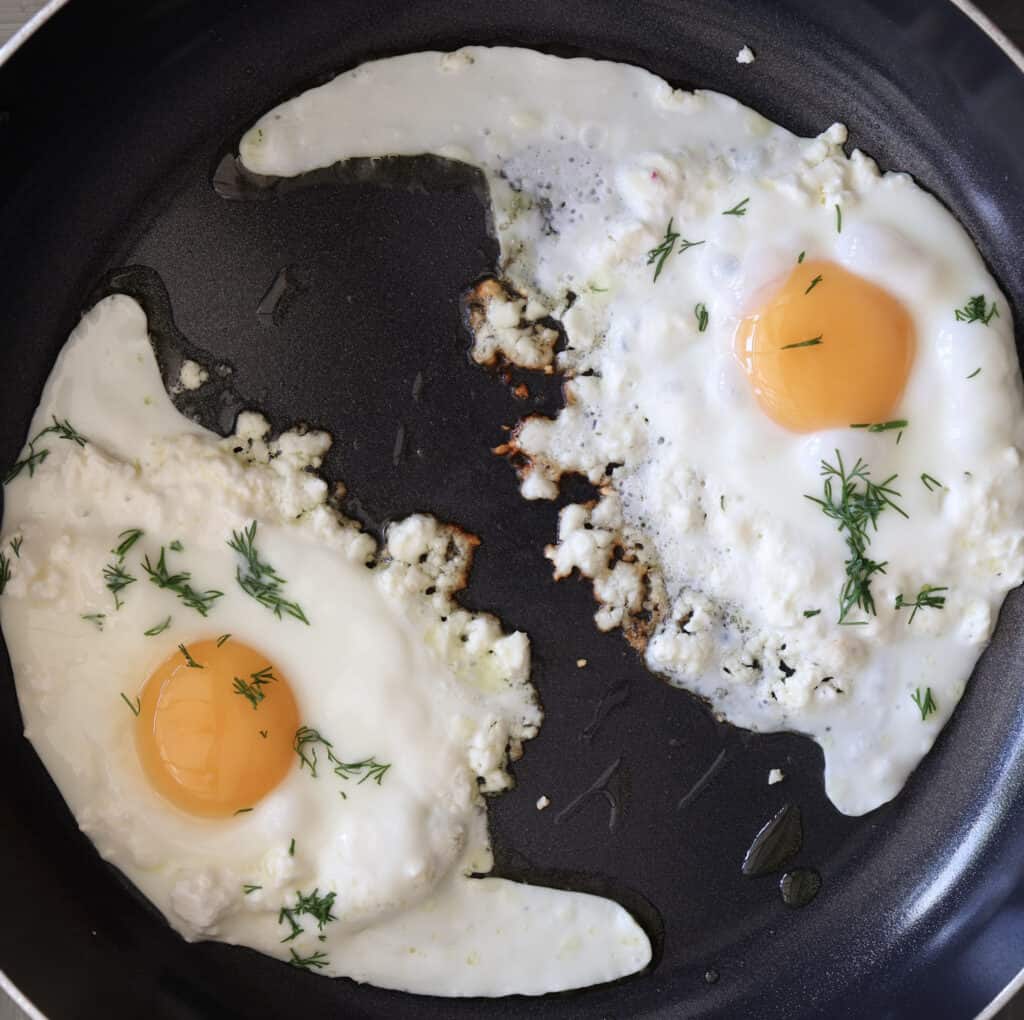 Feta fried eggs cooking in a skillet.