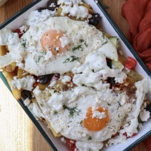 Loaded Mediterranean breakfast fries with feta fried eggs on a serving plate.