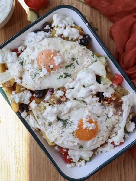 Loaded Mediterranean breakfast fries with feta fried eggs on a serving plate.