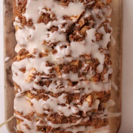 Glazed apple fritter bread with cinnamon streusel sitting on a cutting board ready to be sliced.