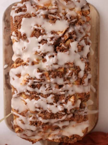 Glazed apple fritter bread with cinnamon streusel sitting on a cutting board ready to be sliced.