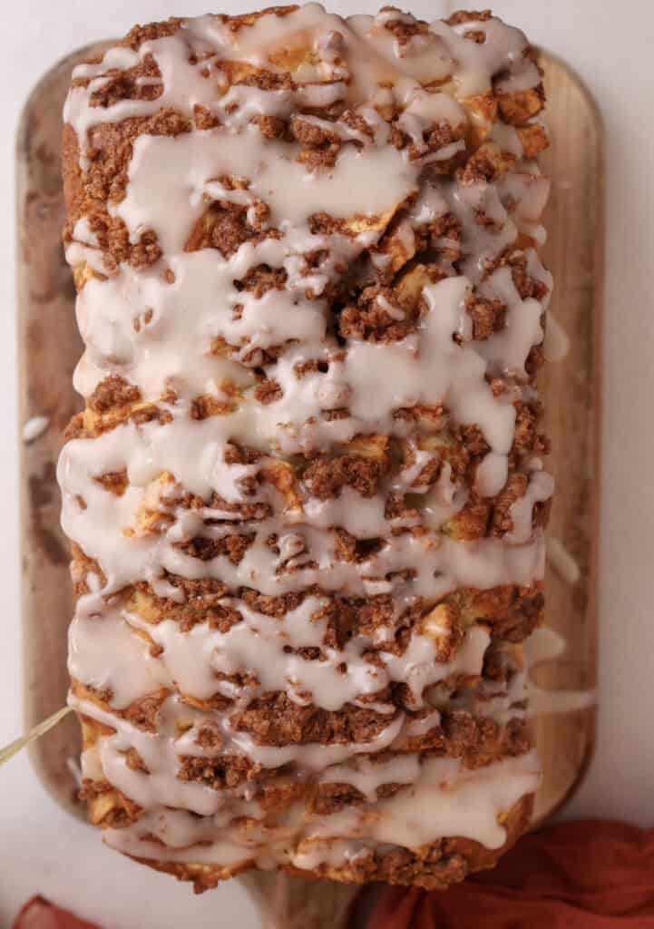 Glazed apple fritter bread with cinnamon streusel sitting on a cutting board ready to be sliced.
