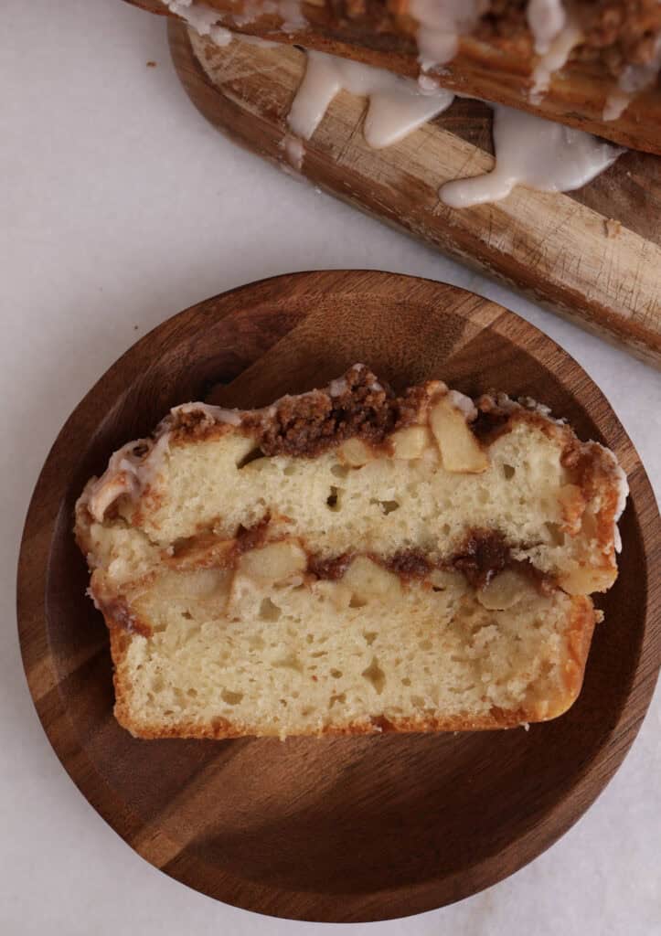 Slice of apple fritter bread on a wood plate, showing the diced apples and cinnamon streusel running through the middle of the slice. 