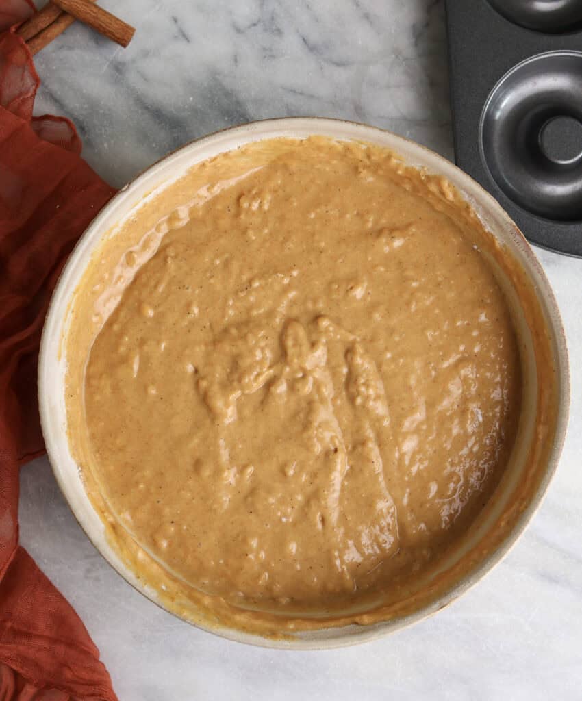 Pumpkin donut batter in a bowl next to a donut tin pan.